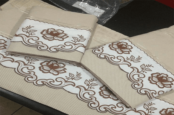 Elegant floral embroidery design on beige and white fabric with intricate flower outlines.