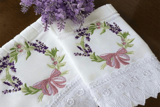 Lavender embroidery design on white fabric with floral wreath and pink bow.